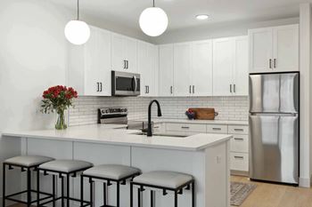 a large kitchen with white cabinets and a counter with three stools